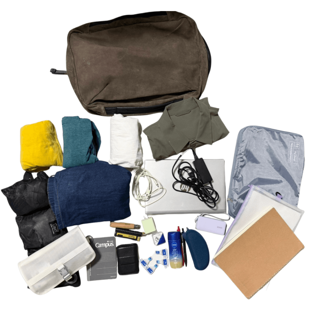 Brown backpack with clothes, toiletries, electronics, and packing items laid out for travel.