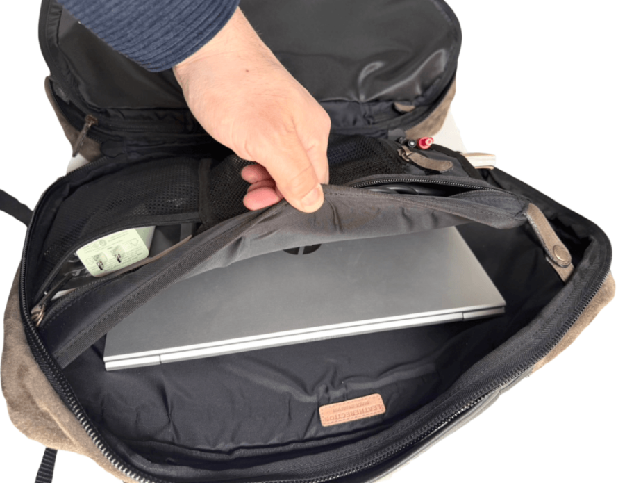 Backpack opened to show a closed laptop in a padded sleeve inside the main compartment, with a hand lifting the zipper pull.
