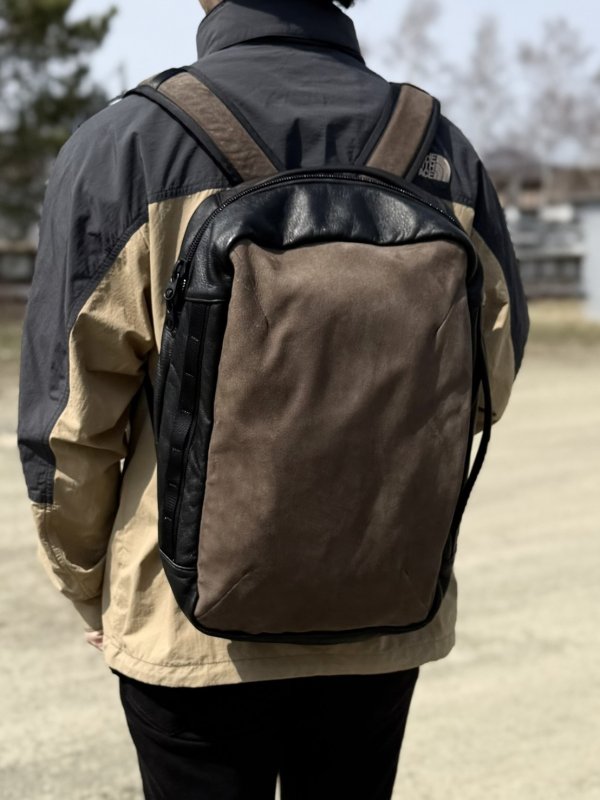 Person seen from behind wearing a two-tone brown and black backpack outdoors.