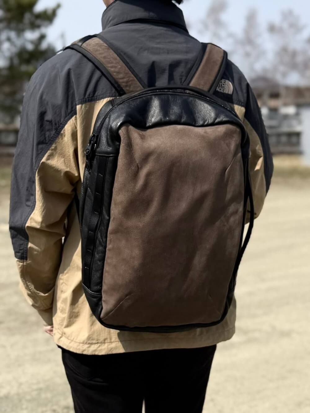 Person seen from behind wearing a two-tone brown and black backpack outdoors.