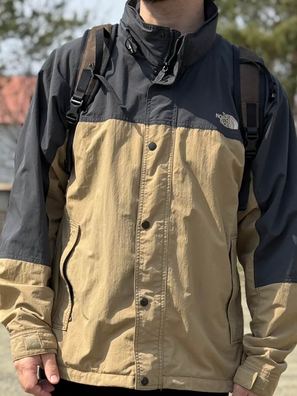 Person wearing a two-tone beige and black North Face outdoor jacket with backpack straps outdoors.
