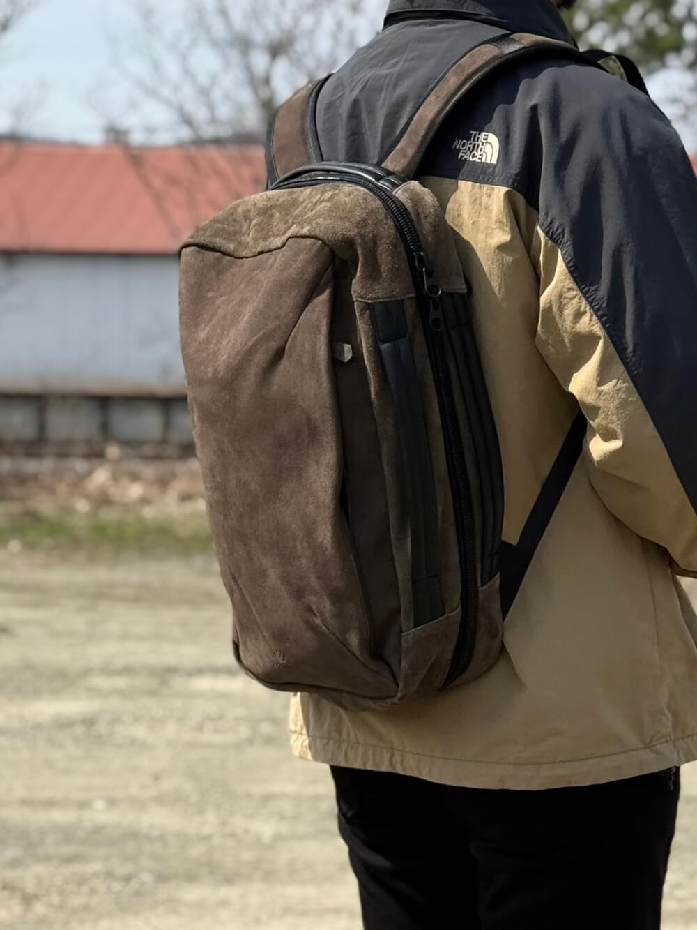 Person seen from behind wearing a two-tone North Face jacket and carrying a large brown backpack outdoors.
