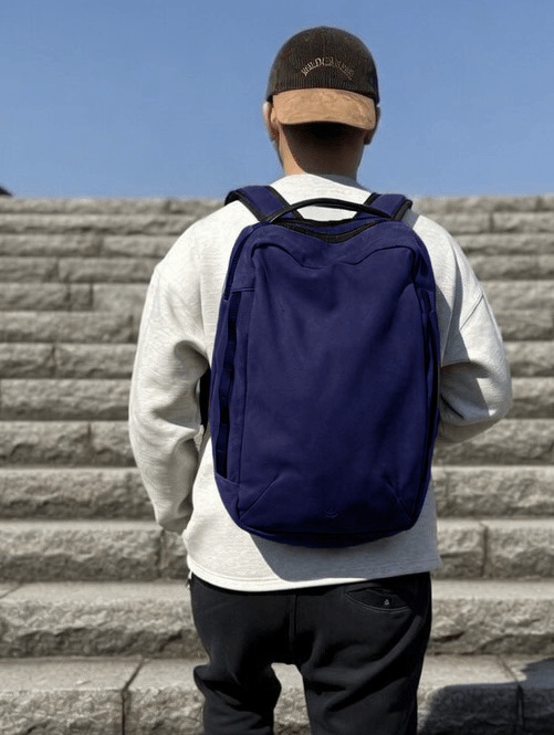 Person wearing a gray hoodie and cap ascending stone steps with a large navy backpack on their back.