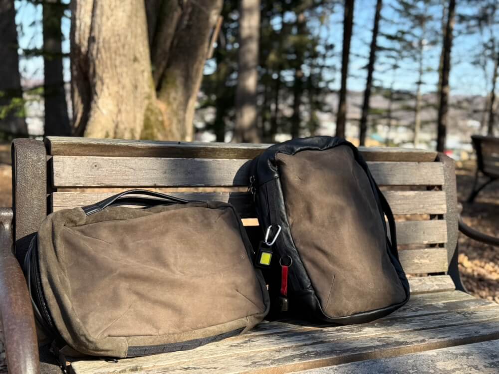 Two brown bags on a weathered park bench outdoors with trees in the background.