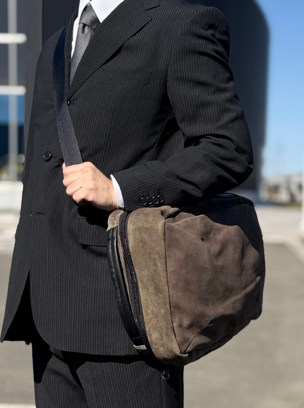 Man in a pinstripe suit carrying a brown suede duffel bag over his shoulder.