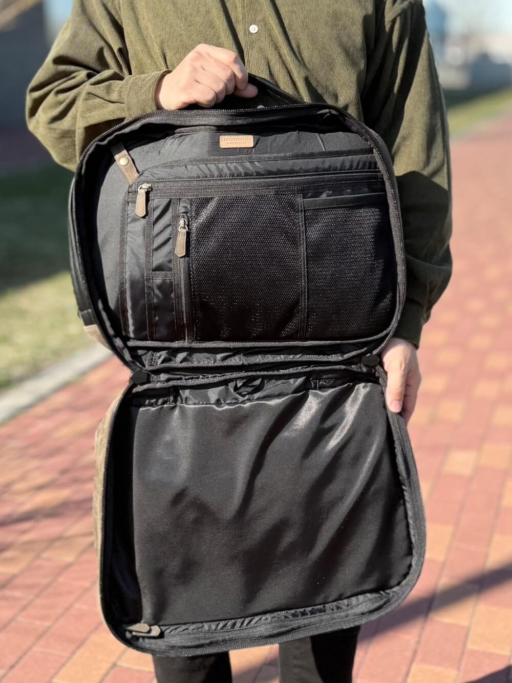 Person opens a black backpack, revealing multiple inner pockets and zippers for organization.