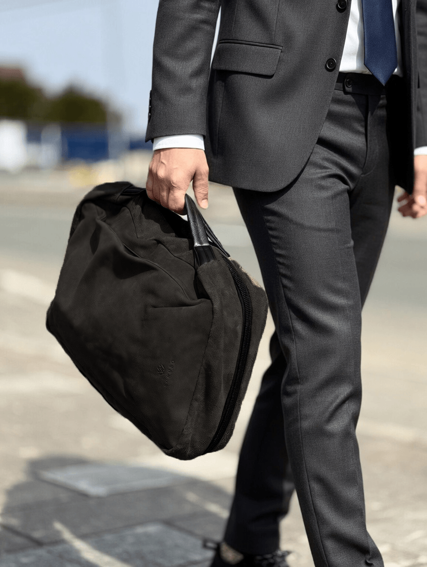 Businessperson in a gray suit carrying a black duffel bag while walking on a sidewalk.
