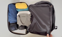 Open suitcase packed with folded clothes (jeans, shirt, hat) being closed by hand.