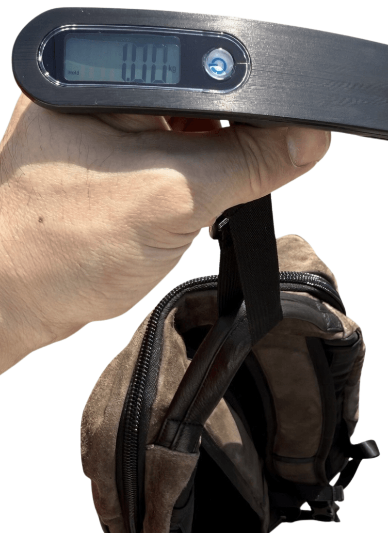 Close-up of a hand holding a digital luggage scale attached to a brown backpack